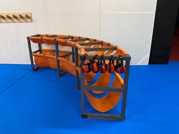 A curved steel frame with bright orange cloth holders for shoes, and some ear defenders.