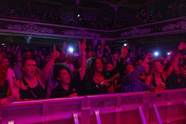 A crowd of people all dancing with their arms in the air, at the barriers of a music event