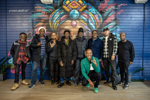 A group of men all posing in front of a grafitti art piece