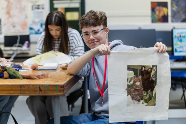 A teen boy holding his design up smiling