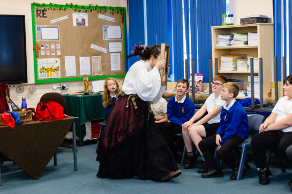 A lady leading a workshop to a group of primary school children, she is holding a picture over her face