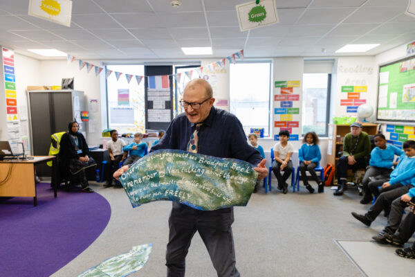 A man hosting a workshop holding a large painting to a primary school class