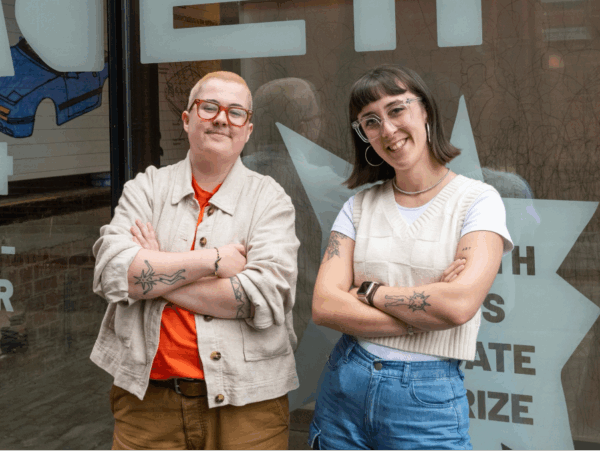 Two people stood against a wall smiling