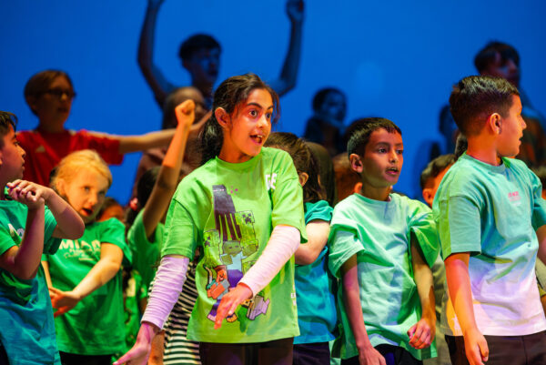 Young children in green t-shirts singing and dancing on satge