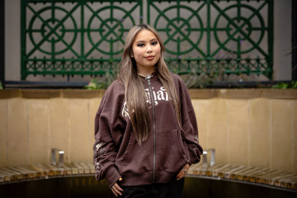 Image of a young woman posing, smiling towards the camera, in front of lareg green gates