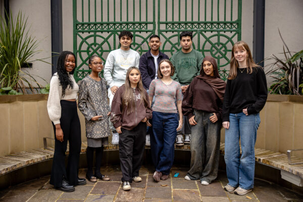 Young people all posing together for a photo outside in front of large green gates