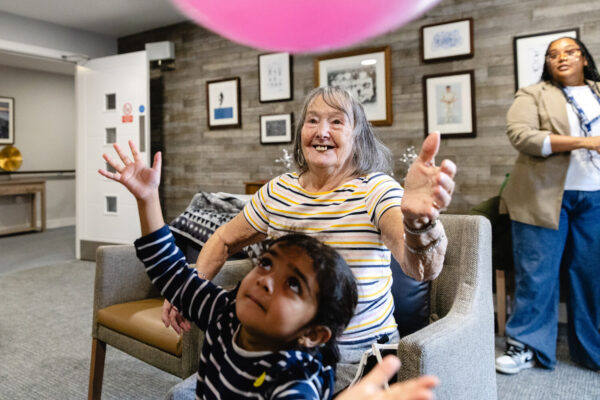 An elderly lady playing with a large colourful ball a young girl