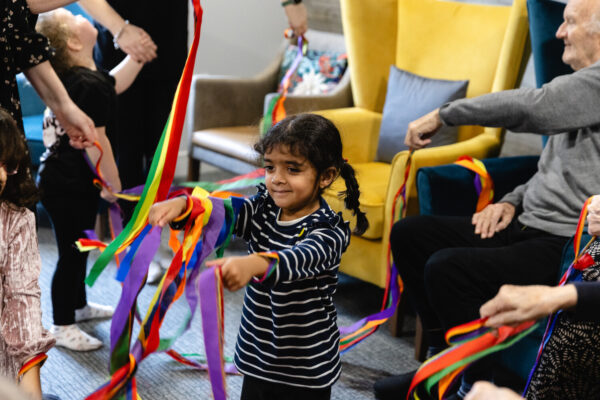 A young girl playing with colourful tissue strips in an elderly home
