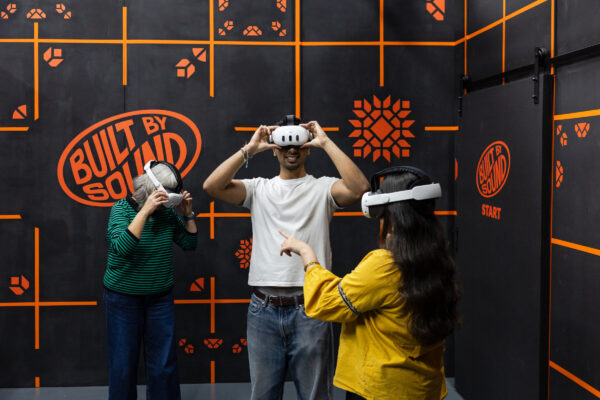 Three young people with VR headsets on in an orange and black room.