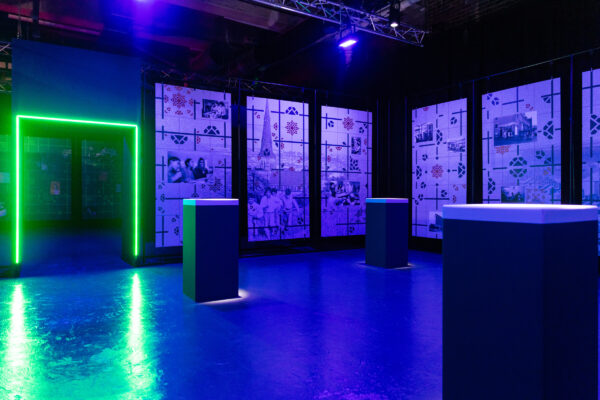 A glowing green doorway on the left, with three posts around the room in the basement of Loading Bay.