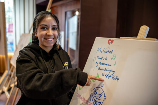 Girl smiling at the camera, pointing at notes on a board