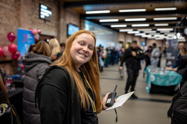 a young woman smiling at the camera, holding a walkie talkie