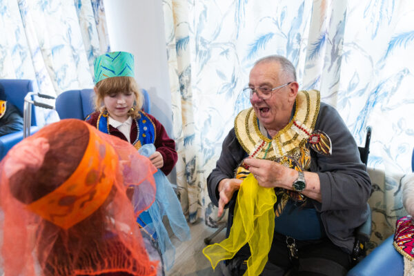 An elderly man playing dress up with young children in a care home