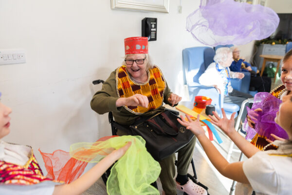 An elderly lady playing dress up and dancing with young girls