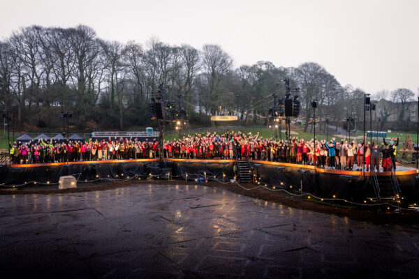 A large group of people stood on a stage celebrating with their hands in the air.