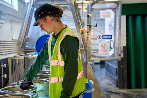 A man standing in a factory with his hand on a beer casket.