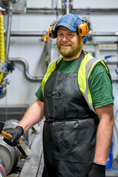 A man with a beard smiles while working in a factory.