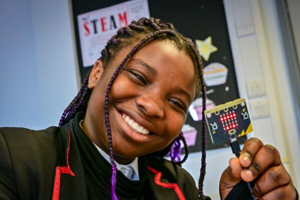 A smiling girl holds up a small object with LED lights.