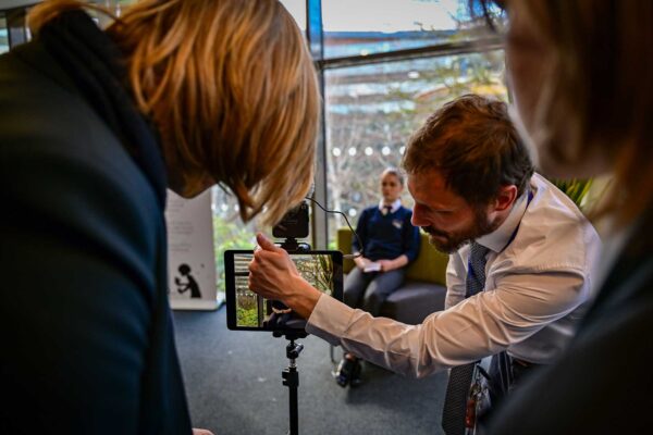 A teacher shows a young person how to use an ipad, connected to a tripod, in a creative workshop.