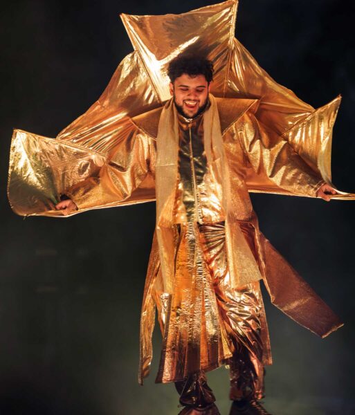 A performer in a bright gold costume smiles.