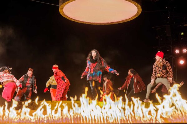 Performers on a stage, with a ring of fire below their feet.