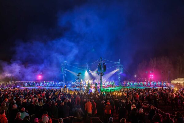A wide shot of the Brighter Still stage, full of smiling performers and lights. There is a large crowd surrounding the stage.