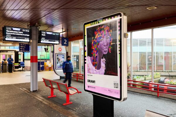A poster in a train station. There is a drawing on the poster of a woman with colourful hair.