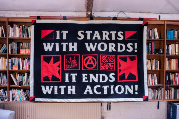Large black and red banner reading “It starts with words! It ends with action!” hanging in front of bookshelves.