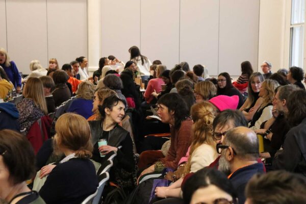 A large group of people sitting in rows at a conference, chatting in between talks.